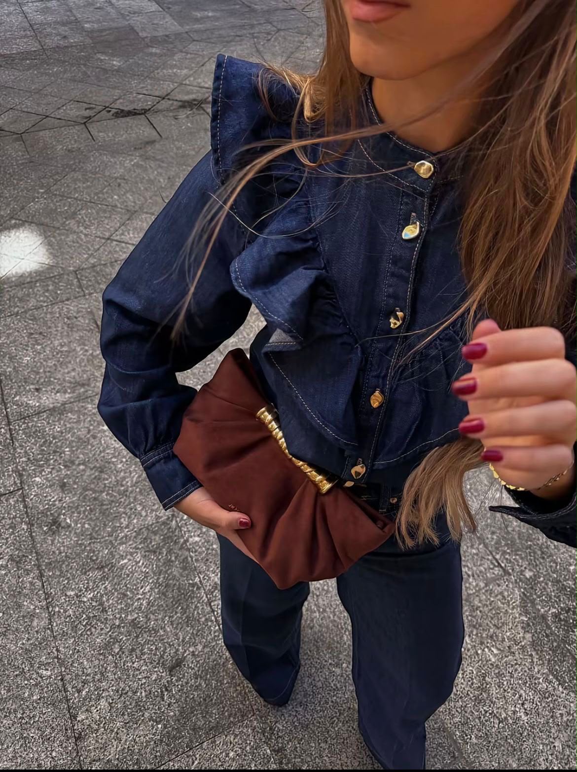 Blusa Merano em denim azul-escuro com folhos nos ombros, botões dourados e mangas compridas, combinada com calças claras.