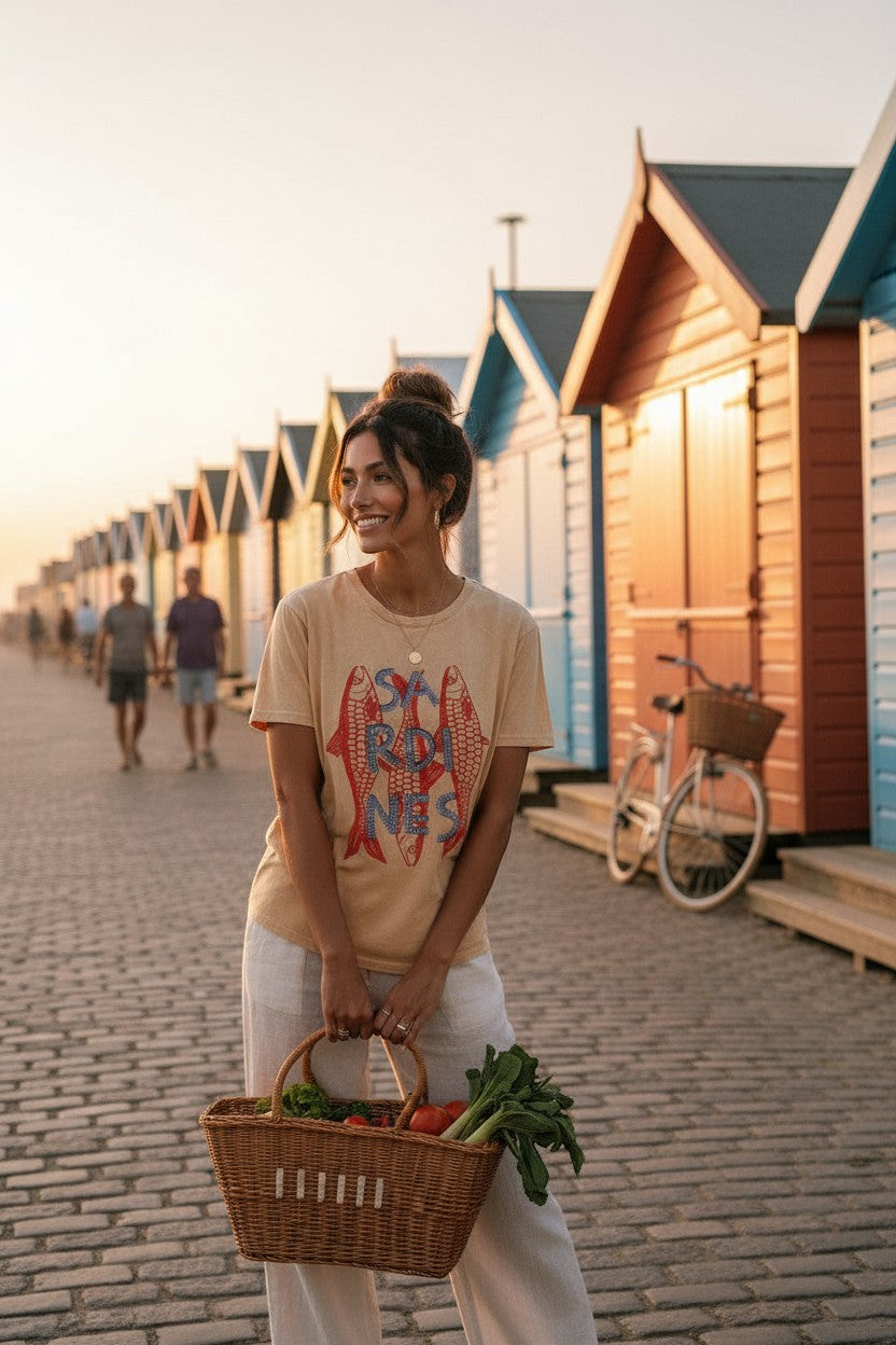 shevibes sandy beige cotton t-shirt with red fish graphic and "SARDINES" text. Model wears it with white linen pants.