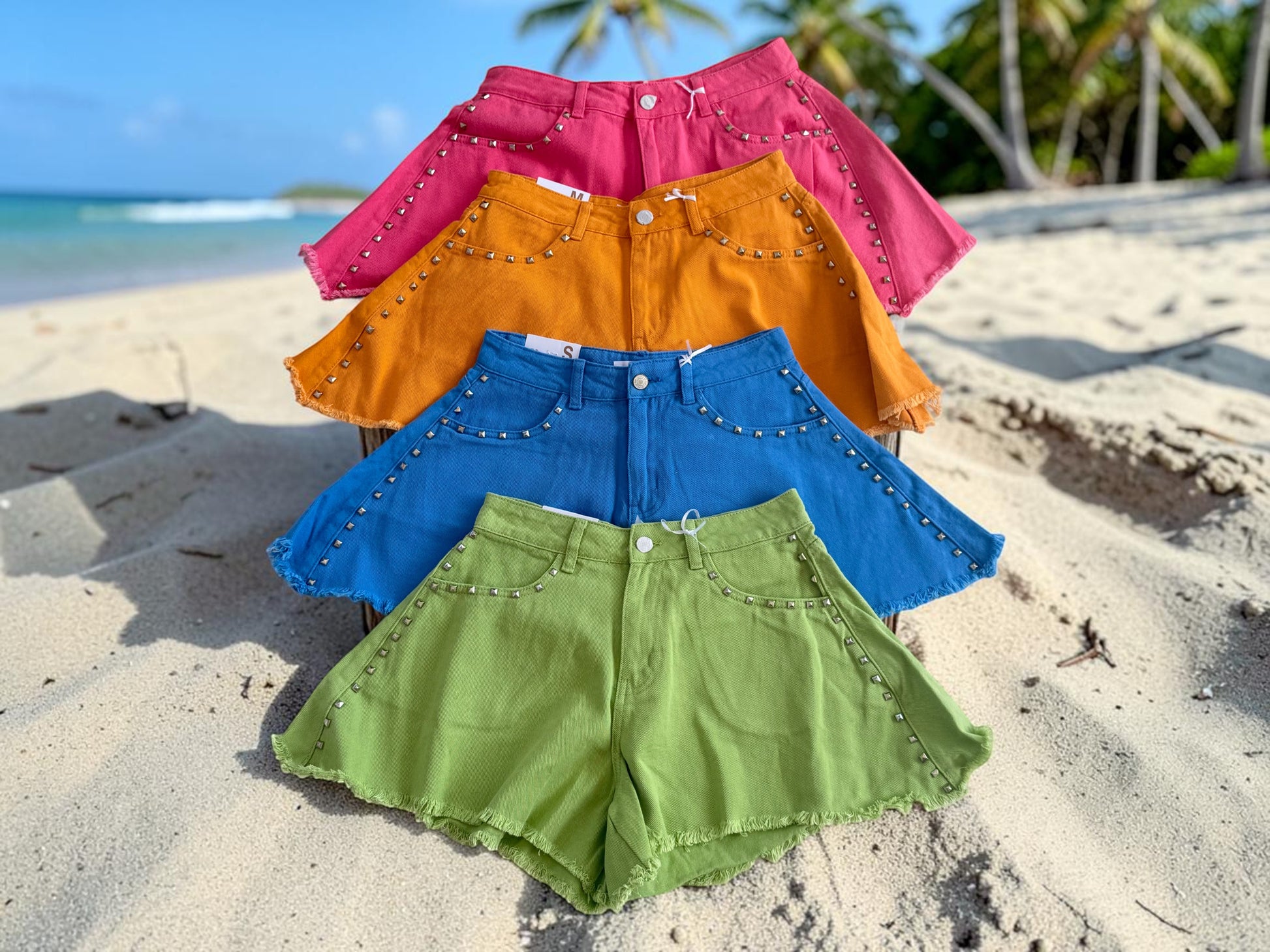 shevibes four colorful denim shorts with studded trim and frayed hems displayed on a sandy beach